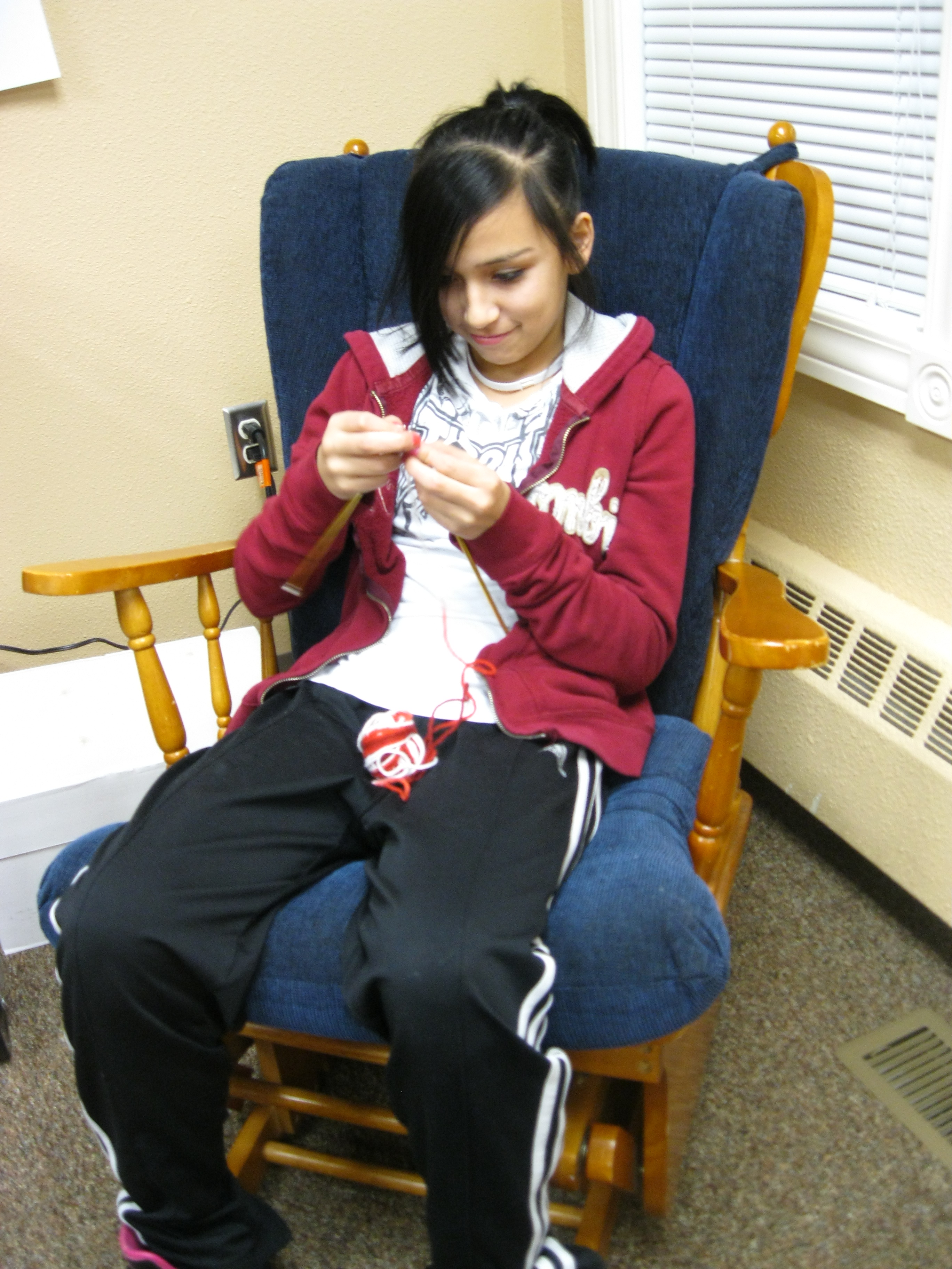 Lakota (Sioux) child knitting in a rocking chair.