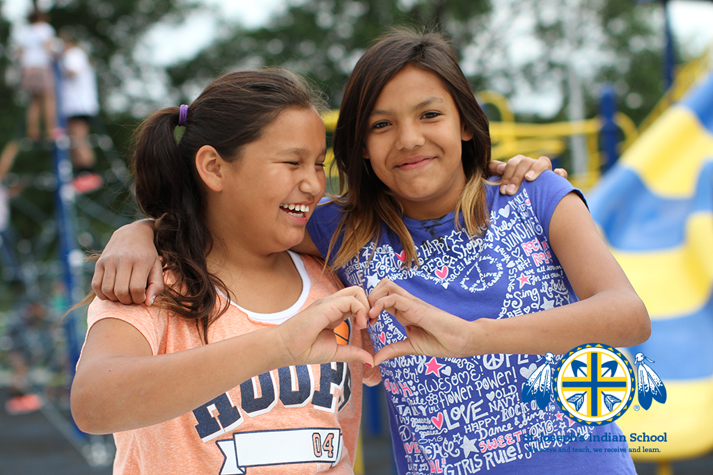 Two girls create a heart shape with their hands on the playground