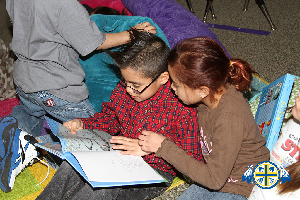 Two Lakota students sit on the ground reading a book. 