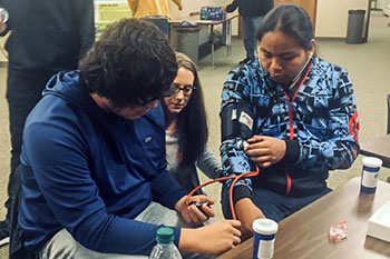 Two St. Joseph’s high school students practice monitoring each other’s blood pressure under the guidance of an SDUS Pharmacy student. 